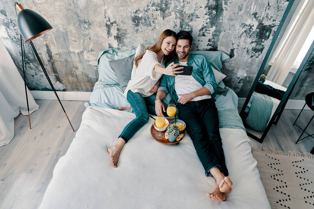 Giovane coppia caucasica trascorrere del tempo a letto con la prima colazione, succo d'arancia e la navigazione cellulare
   - Foto, immagini