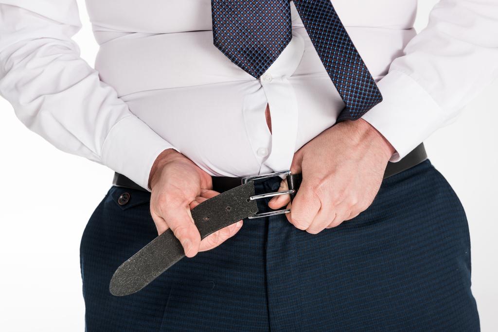 vista parcial del hombre con sobrepeso en ropa formal poniéndose pantalones ajustados aislados en blanco
 - Foto, imagen