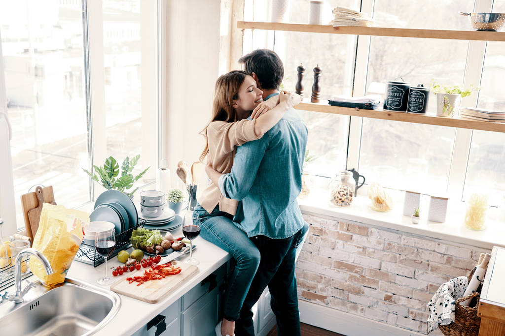 Rakkautta on ilmassa. Kaunis nuori pari syleilee seistessään keittiössä kotona
 - Valokuva, kuva