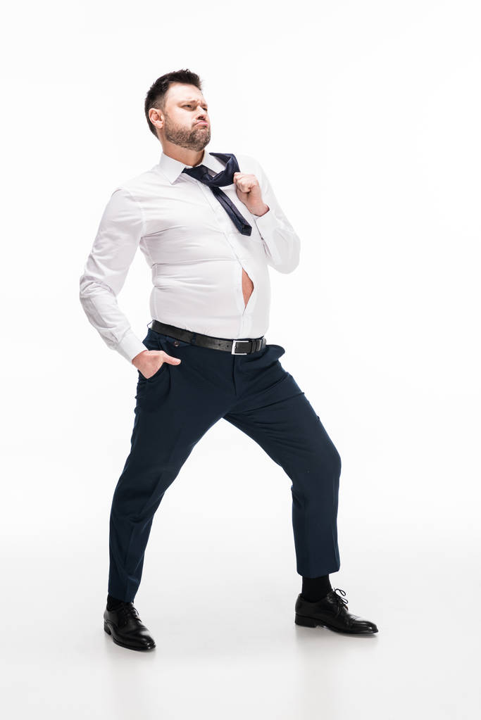 υπέρβαρο άνθρωπος σε σφιχτό επίσημο ντύσιμο με το χέρι στην τσέπη που ποζάρει σε λευκό - Φωτογραφία, εικόνα