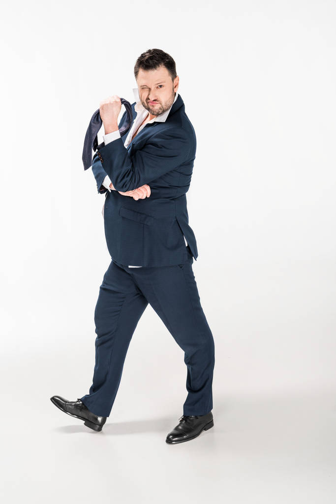 overgewicht man in strakke formele slijtage Holding stropdas, winking en kijken naar camera op wit - Foto, afbeelding
