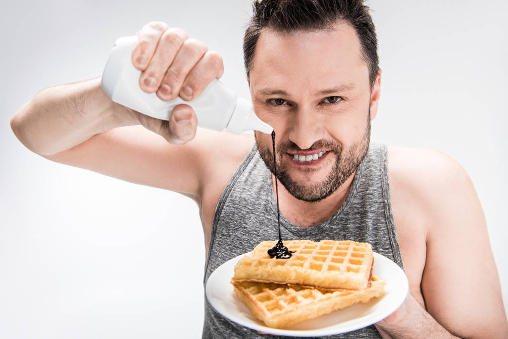 smiling chubby man pouring chocolate syrup on waffles on white - Photo, Image