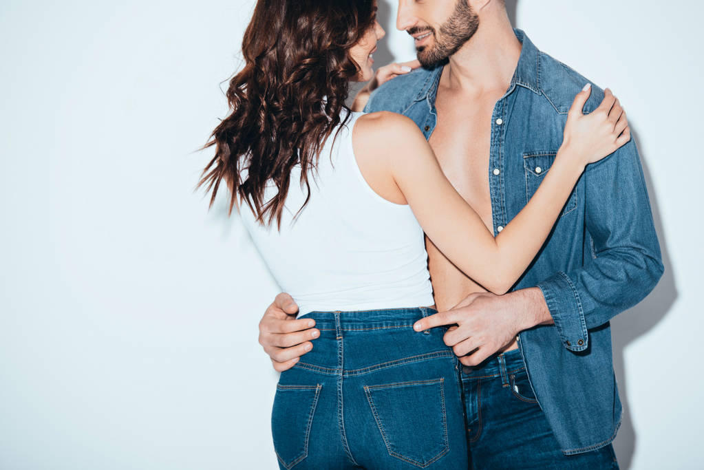 recortado vista de sonriente pareja en jeans abrazando en gris
 - Foto, Imagen