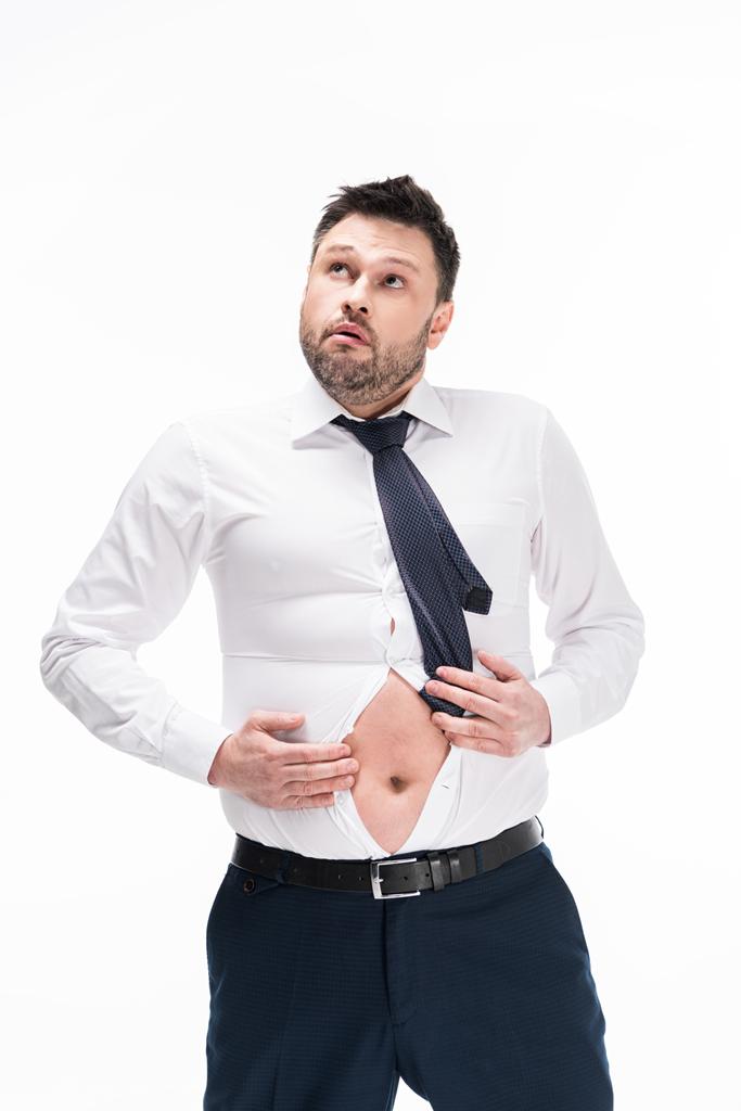 übergewichtiger Mann in enger formaler Kleidung, der wegschaut, während er Bauch isoliert auf Weiß zeigt - Foto, Bild