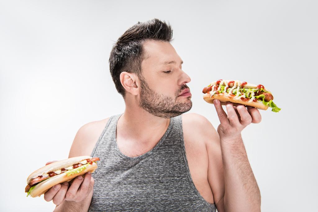 Избыточный вес человек нюхающий аромат хот-дога изолированы на белом
 - Фото, изображение
