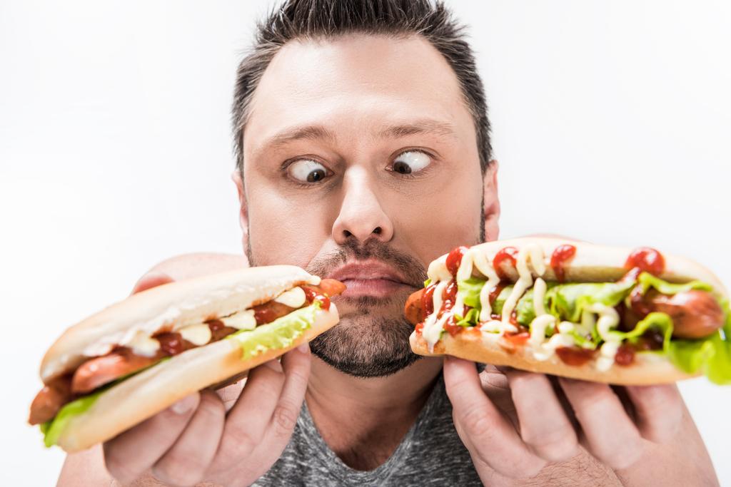l'uomo in sovrappeso che tiene gli hot dog e rende l'espressione del viso isolata sul bianco
 - Foto, immagini