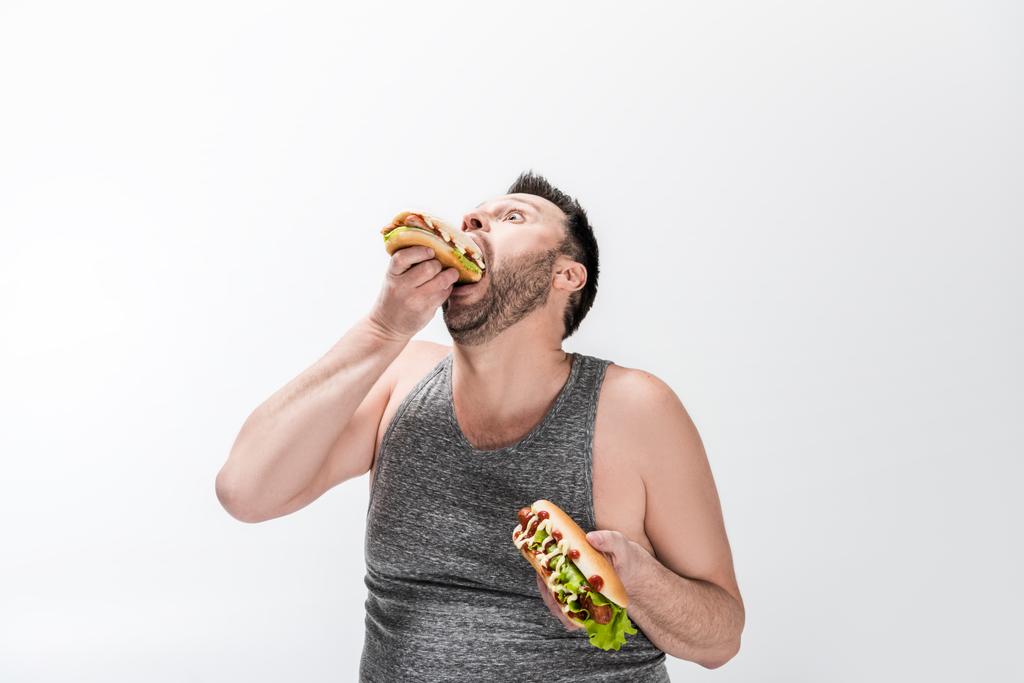 Hungriger übergewichtiger Mann im Tanktop isst Hot Dog auf Weiß - Foto, Bild