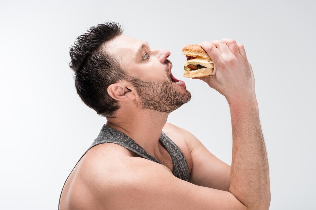side view of chubby bearded man eating burger isolated on white - Photo, Image