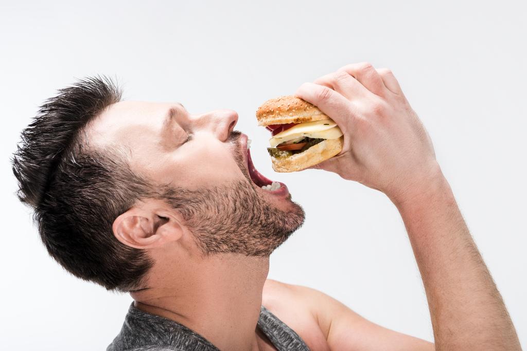 вид збоку пухкий бородатий чоловік їсть смачний бургер ізольований на білому
 - Фото, зображення