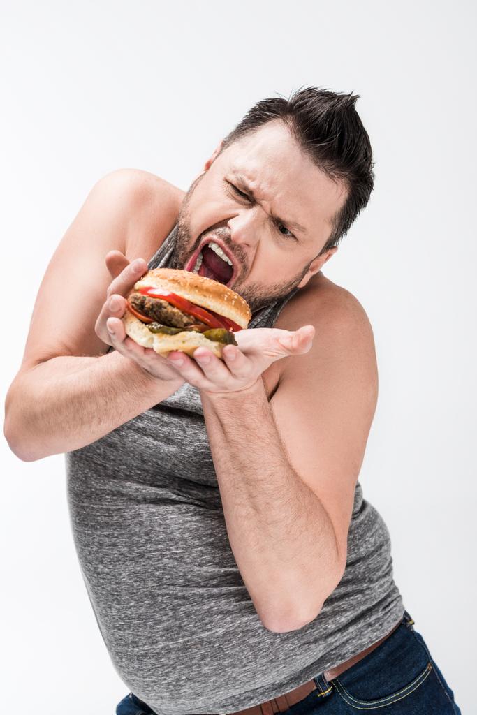 hombre con sobrepeso haciendo expresión de la cara mientras posando con hamburguesa aislada en blanco
 - Foto, imagen
