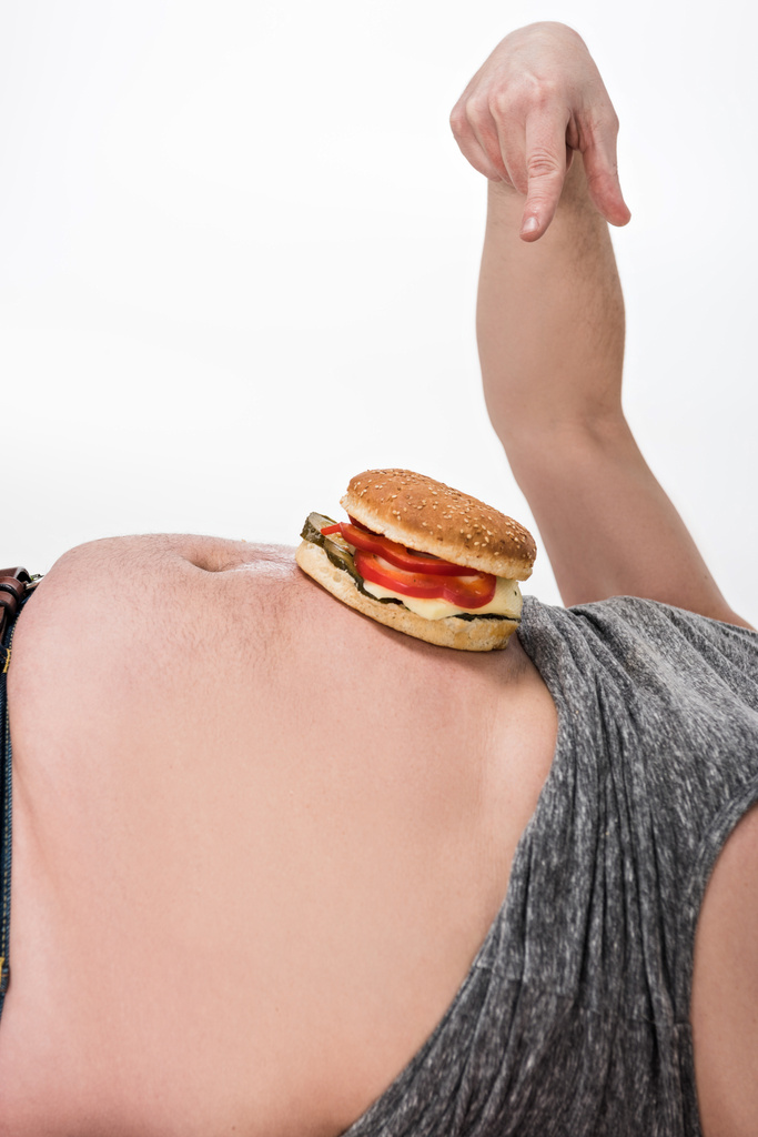 vue recadrée de l'homme en surpoids pointant avec le doigt au hamburger sur le ventre isolé sur blanc
 - Photo, image