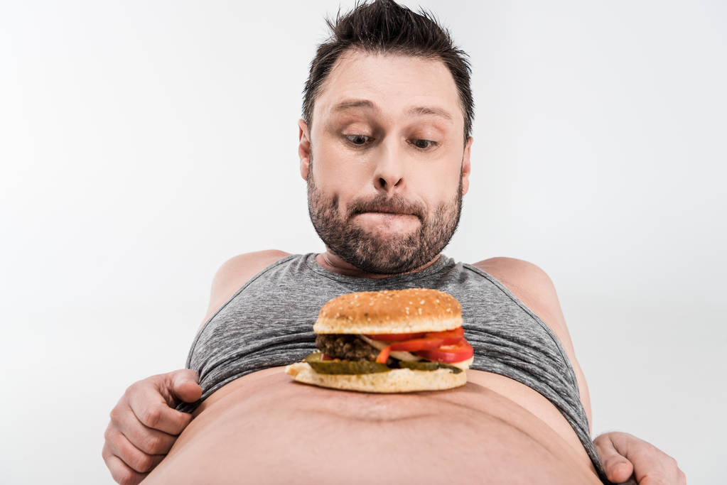 Übergewichtiger Mann sieht Burger auf Bauch isoliert auf weißem Grund - Foto, Bild