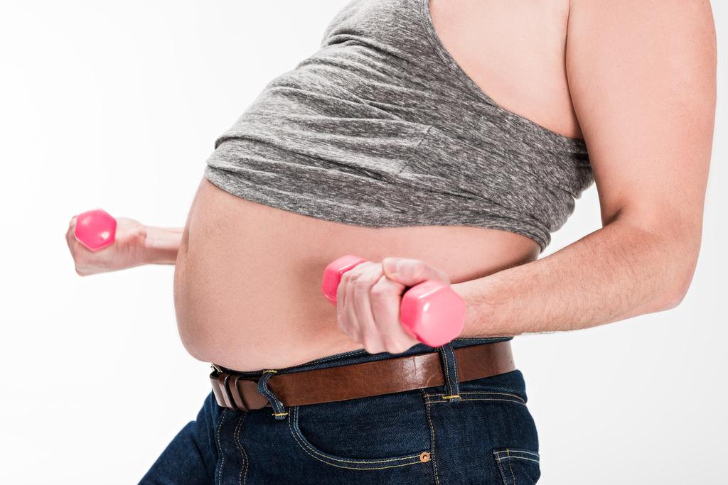 vista recortada del hombre con sobrepeso mostrando el vientre y haciendo ejercicio con pesas rosadas aisladas en blanco
 - Foto, Imagen
