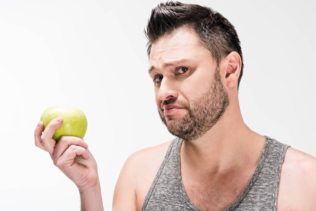 unzufriedener pummeliger Mann hält grünen Apfel in der Hand und blickt isoliert auf weiße Kamera - Foto, Bild