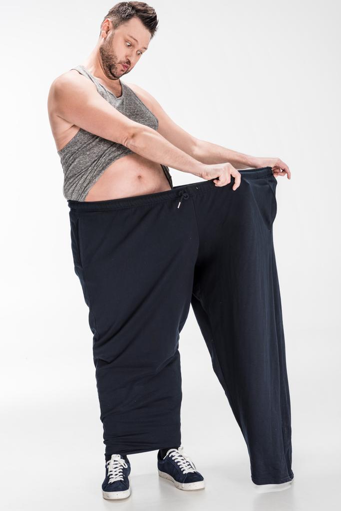 homem sobrepeso surpreso segurando calças grandes após a perda de peso no branco
 - Foto, Imagem