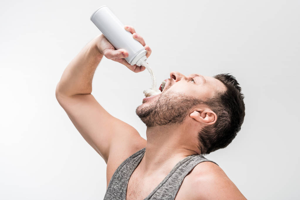 пухлый мужчина в майке распыляет взбитые сливки во рту на белый
 - Фото, изображение