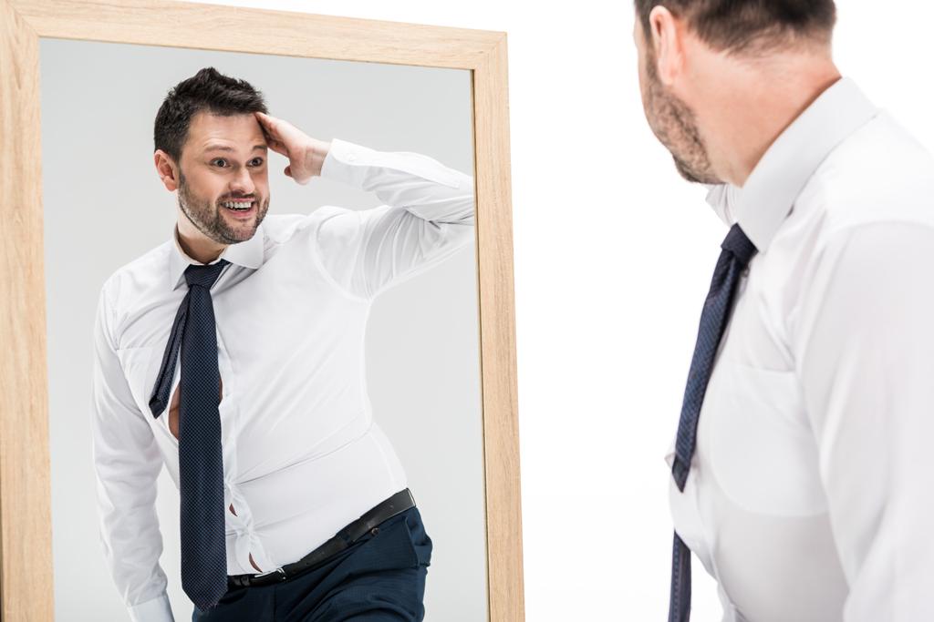 uomo in sovrappeso sorridente in abbigliamento formale guardando riflesso in specchio isolato su bianco
 - Foto, immagini