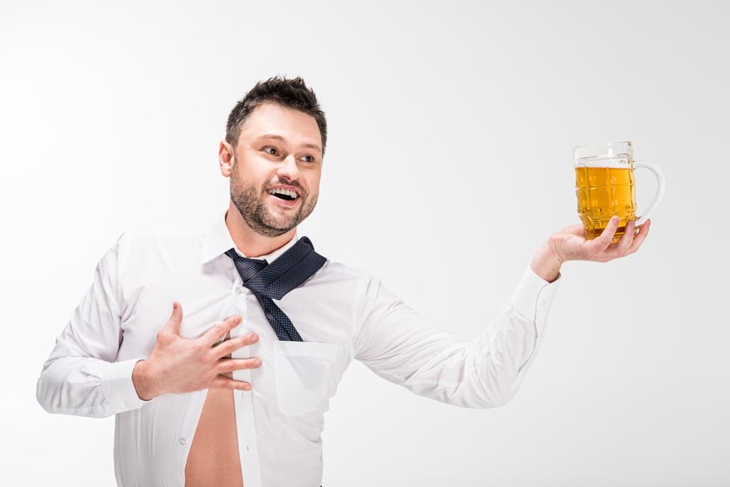 glücklicher übergewichtiger Mann im engen Hemd mit einem Glas Bier in der Hand und gestikulierend mit einer Hand auf weißem Hintergrund - Foto, Bild
