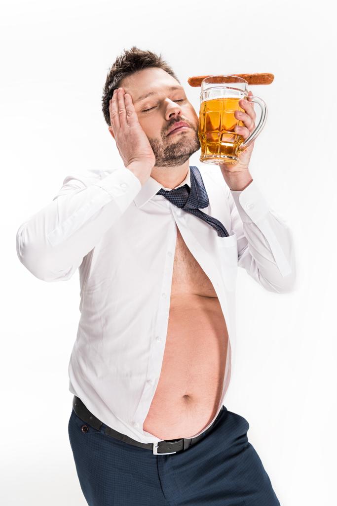 ソーセージでビールのグラスを持ち、目を閉じて白でポーズをとる太りすぎの男 - 写真・画像