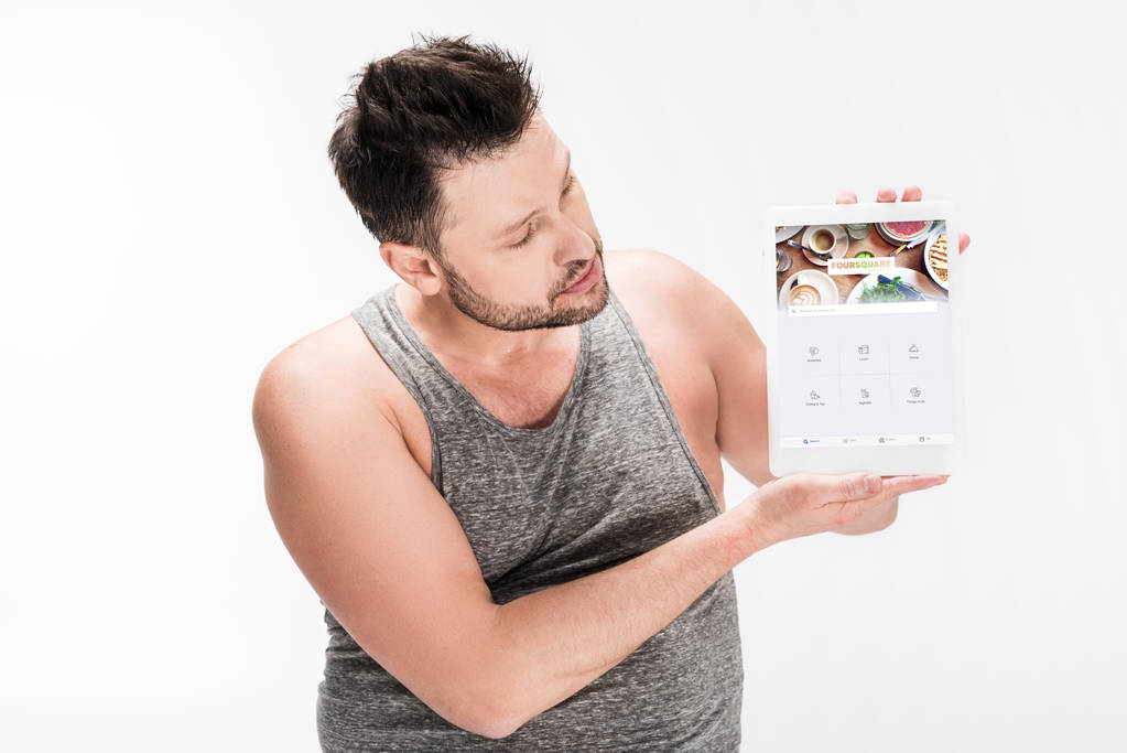 Человек с избыточным весом показывает цифровой планшет с четырехквадратным приложением на экране изолированы на белом
 - Фото, изображение