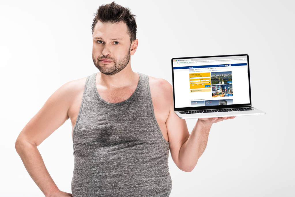 człowiek z nadwagą patrząc na kamerę i trzymając laptopa z witryną rezerwacji na ekranie białym na białym tle - Zdjęcie, obraz