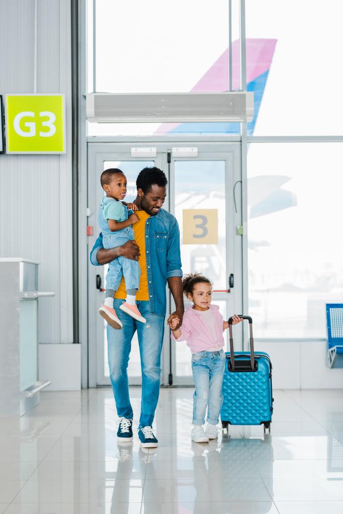 havaalanında bekleyen salon boyunca çocuk ve Bagaj ile yürüyen Afrikalı Amerikalı baba gülümseyen - Fotoğraf, Görsel