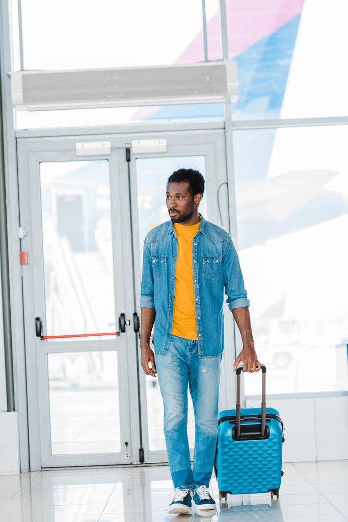 афроамериканський чоловік ходить з валізою уздовж залу очікування в аеропорту
 - Фото, зображення