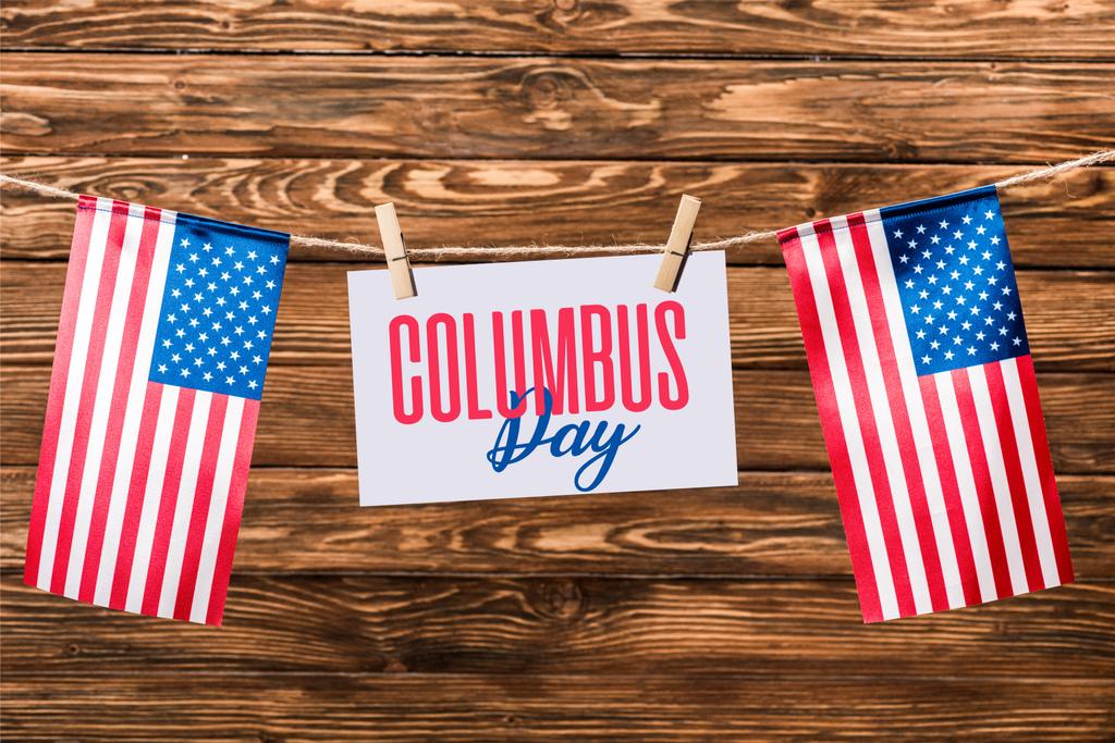 κάρτα με Columbus day γράμματα κρέμονται συμβολοσειρά με καρφίτσες και αμερικανικές σημαίες σε φόντο ξύλινη - Φωτογραφία, εικόνα