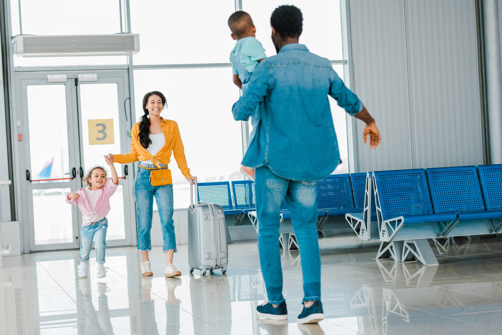 afro-americana feliz mulher com filha andando em direção marido com filho no aeroporto
 - Foto, Imagem