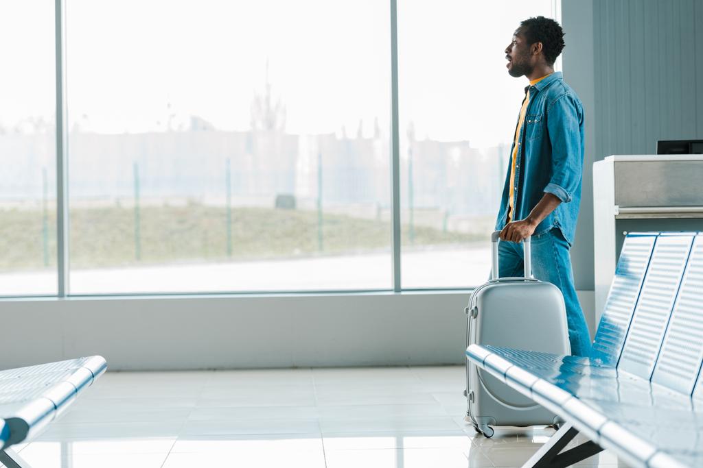 vue latérale de l'homme afro-américain marchant seul avec valise à l'aéroport
 - Photo, image
