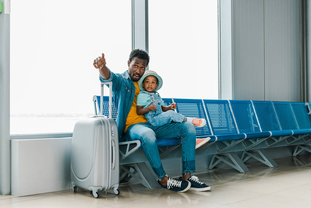 Afrikkalainen amerikkalainen isä istuu pojan kanssa lentokentällä ja osoittaa sormella pois
 - Valokuva, kuva