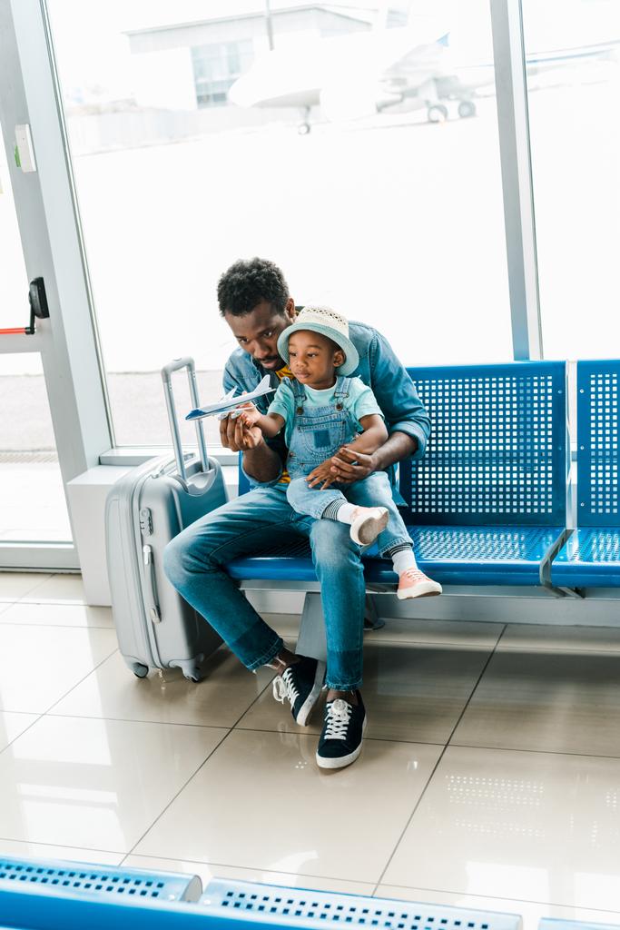 afro-americano pai e filho sentado com mala na sala de espera no aeroporto e brincando com avião de brinquedo
 - Foto, Imagem