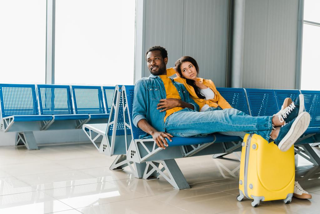 κουρασμένο αφρικανικό ζευγάρι που κάθεται στο σαλόνι αναχώρησης με βαλίτσα και περιμένει για την πτήση - Φωτογραφία, εικόνα