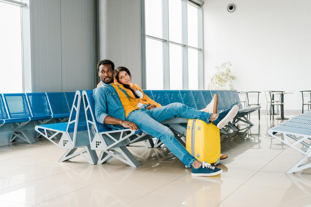 vyčerpaná africká americká dvojice, která sedí v hale s kufříkem a čeká na útěk - Fotografie, Obrázek