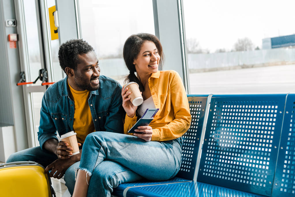 onnellinen afrikkalainen amerikkalainen pari istuu lähtöaulassa kahvia mennä ja lentoliput ja katselee ikkunaa
 - Valokuva, kuva