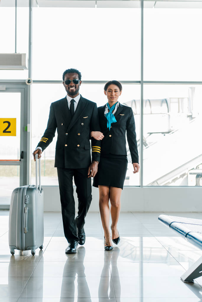 Afrikkalainen amerikkalainen lentäjä ja lentoemäntä kävely yhdessä matkatavaroiden lentokentällä
 - Valokuva, kuva