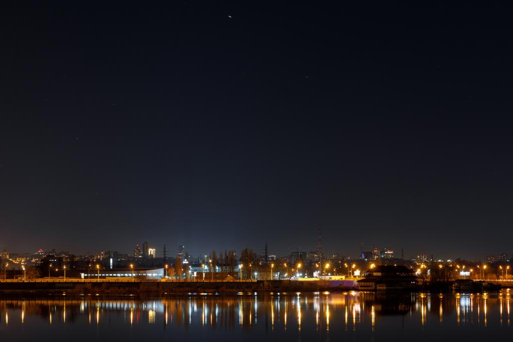 dunkles Stadtbild mit Gebäuden, Lichtern und Fluss bei Nacht - Foto, Bild