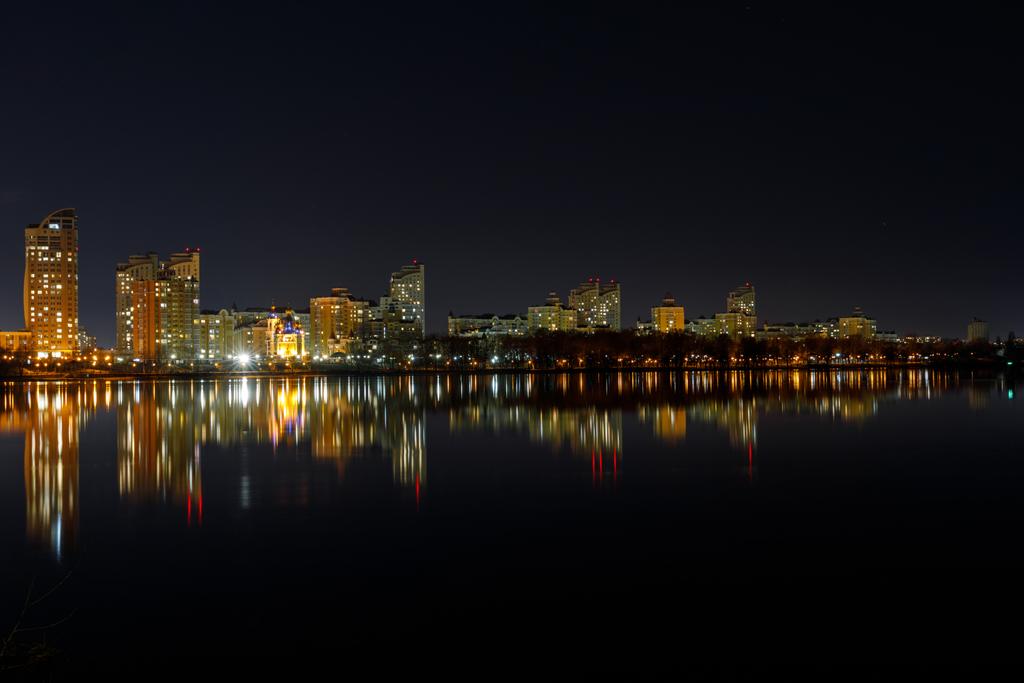 maalauksellinen tumma kaupunkikuva valaistuilla rakennuksilla, joki- ja yötaivas
 - Valokuva, kuva
