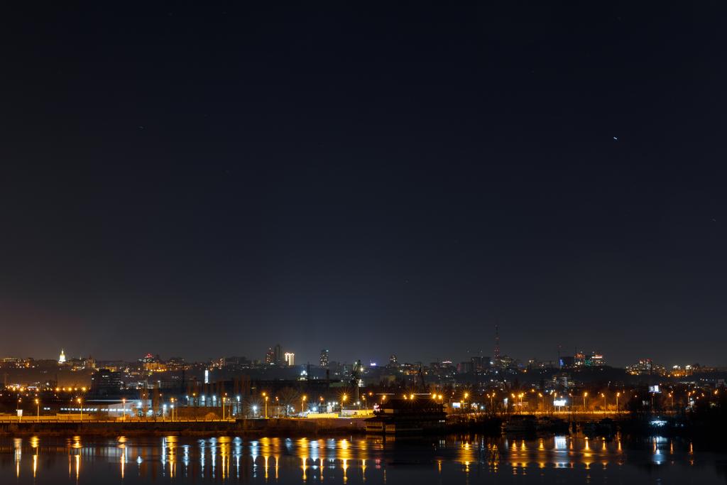 pimeä ja rauhallinen kaupunkikuva valaistuine rakennuksineen ja heijastuksineen joella yöllä
 - Valokuva, kuva