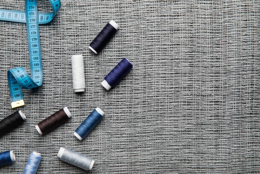 Ansicht von verstreuten blauen und grauen Fadenspulen auf Sacktuch mit Kopierraum und Maßband - Foto, Bild