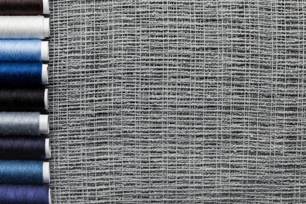 vista superior de bobinas de hilo azul y gris en fila sobre tela de saco con espacio para copiar
 - Foto, Imagen