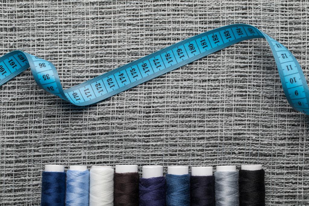 vista superior de bobinas de hilo azul y gris con cinta métrica sobre tela de saco
  - Foto, imagen