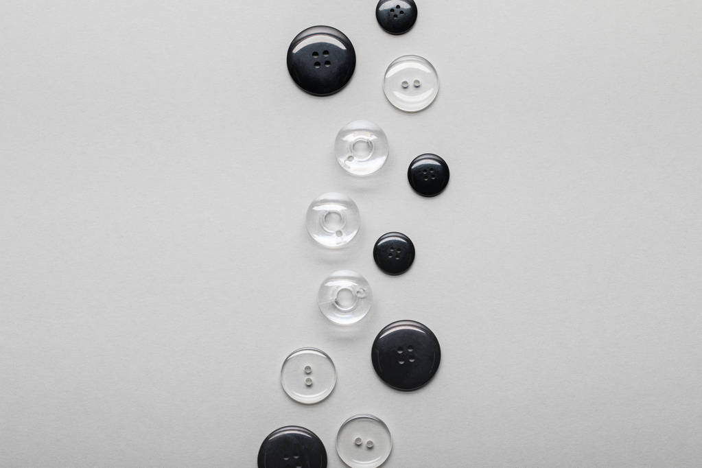 pohled na uspořádání černých a průhledných oděvních tlačítek izolovaných na šedé s prostorem pro kopírování - Fotografie, Obrázek