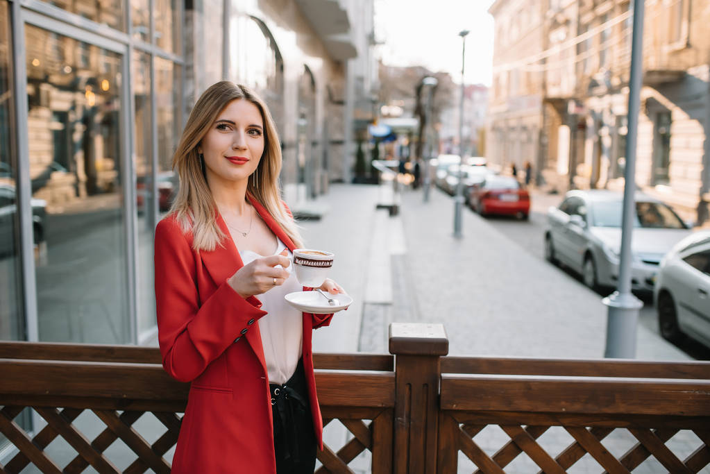 Belle jeune femme d'affaires avec une tasse de café jetable, boire du café, et tenant la tablette dans ses mains sur fond de ville urbaine
. - Photo, image