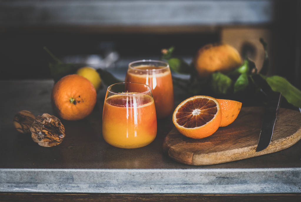 Ποτήρια από φρεσκοστυμμένο χυμό πορτοκαλιού ή αναψυκτικό σε τσιμεντένιο πάγκο κουζίνας. Υγιεινός τρόπος ζωής, χορτοφάγος, χορτοφάγος, αλκαλική δίαιτα, ιδέα για την ανοιξιάτικη αποτοξίνωση - Φωτογραφία, εικόνα