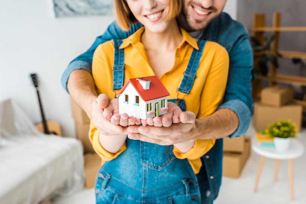Cropped view of smiling couple holding toy house and looking at camera at home - Photo, Image