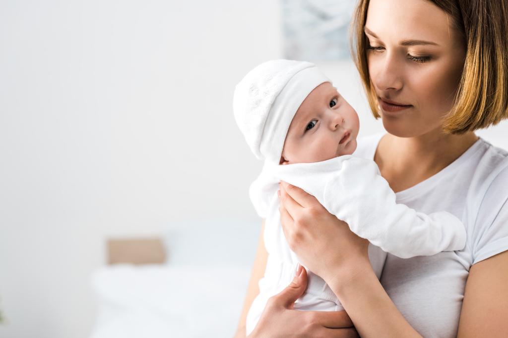 Jonge moeder in wit t-shirt houdt baby thuis - Foto, afbeelding