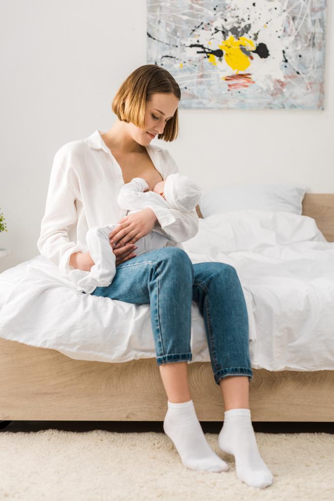 Matka v džínách seděla na posteli a kojila dítě  - Fotografie, Obrázek