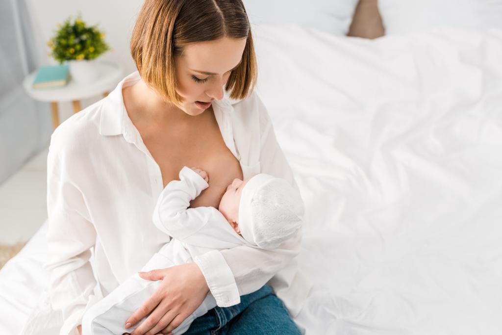 над головой вид молодой матери в белой рубашке грудного вскармливания ребенка дома
 - Фото, изображение