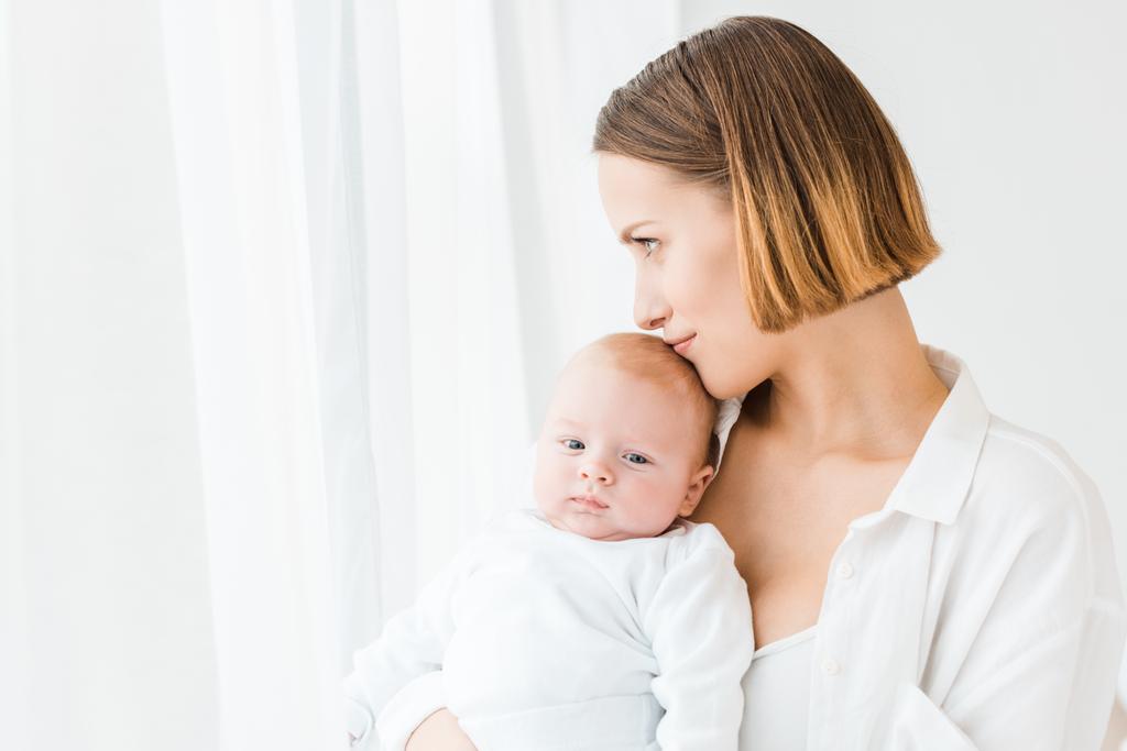 Lächelnde junge Mutter im weißen Hemd mit Baby zu Hause - Foto, Bild